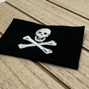 May include: A black fabric patch with a white embroidered skull and crossbones design.