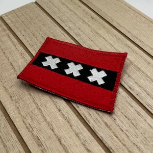 May include: Red fabric patch with three white crosses on a black stripe. The patch is sewn with black thread.