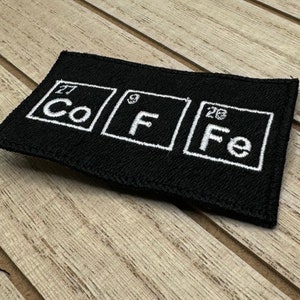 Peut inclure: Patch en tissu noir avec du texte brodé blanc qui lit "Co F Fe" avec les numéros atomiques 27, 9 et 26 au-dessus de chaque symbole d'élément.