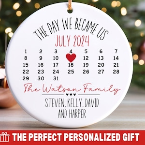May include: White round ornament with black text that reads "The Day We Became Us July 2024" and a calendar with a red heart on the 18th. The text below the calendar reads "The Watson Family Steven, Kelly, David and Harper".