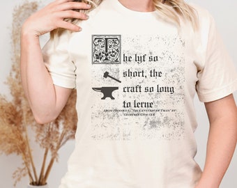 May include: A white t-shirt with a black graphic print of a blacksmith's anvil and hammer. The text reads "he lyf so short, the craft so long to lerne" from "The Canterbury Tales" by Geoffrey Chaucer.