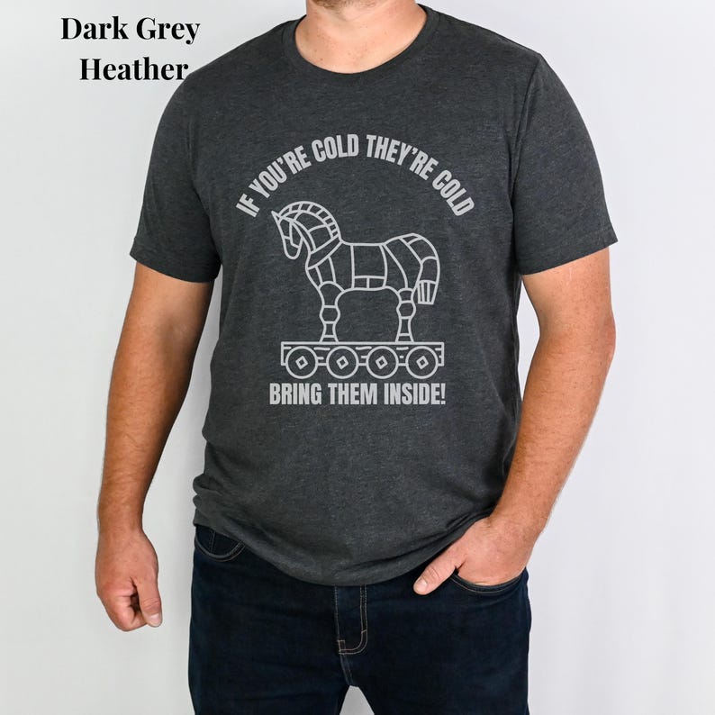 Man wearing a dark grey heather shirt with the words: If your cold they're cold bring them inside! in a white simple font. The words surround a line art image of the Trojan Horse.
