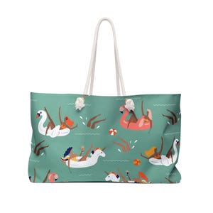 May include: Large teal tote bag with a repeating pattern of people on inflatable swans, flamingos, and unicorns. The bag has white rope handles and a white background. The design includes beach balls and people swimming in the water.