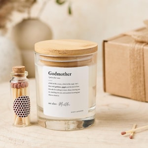 以下が含まれることがあります： 木製の蓋と「Godmother」と書かれたラベルが付いたガラスのキャンドルジャー。マッチの小さなガラス瓶とギフトボックスも付いています。キャンドルはラベンダーの香りです。