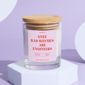 May include: A clear glass candle jar with a wooden lid. The label reads "ONLY BAD BITCHES ARE ENGINEERS" in red text on a pink background. The candle is made of 100% vegan soy wax and has a burn time of 25 hours.