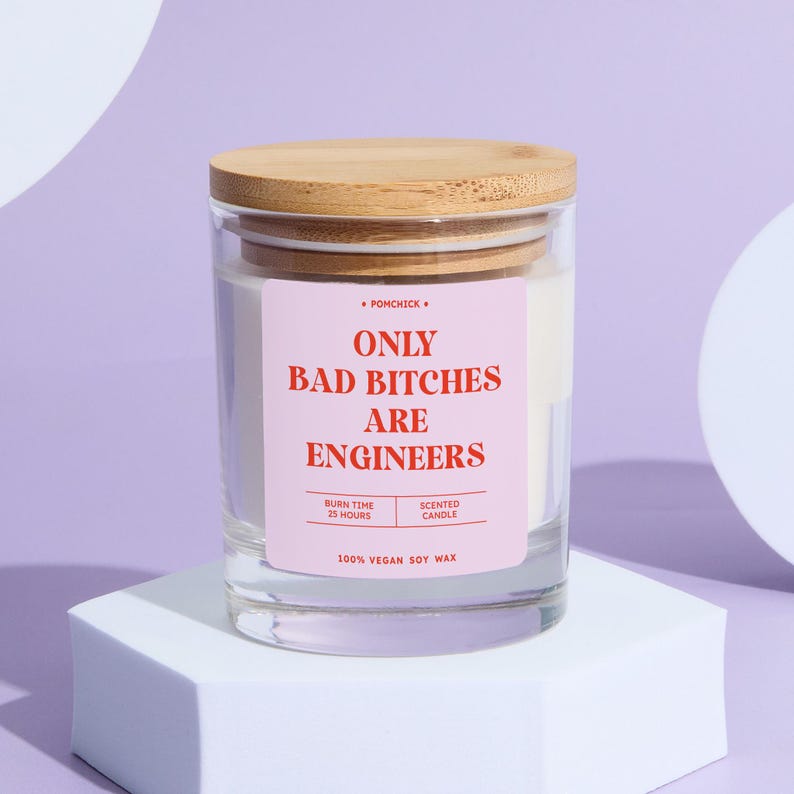 May include: A clear glass candle jar with a wooden lid. The label reads "ONLY BAD BITCHES ARE ENGINEERS" in red text on a pink background. The candle is made of 100% vegan soy wax and has a burn time of 25 hours.