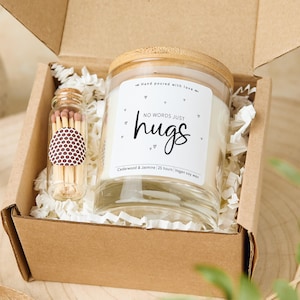 Op de afbeelding: Een cadeau set in een bruine kartonnen doos met een glazen potkaars met een houten deksel en een kleine glazen fles met lucifers. De kaars heeft een label met de tekst "NO WORDS JUST hugs". De kaars is geurend met Cedarwood & Jasmine en gemaakt van vegan sojawas.