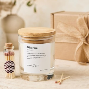 Könnte beinhalten: Ein Glas-Kerzenglas mit Holzdeckel, beschriftet mit "Divorced" und einer Definition. Neben der Kerze steht eine kleine Glasflasche mit Streichhölzern. Die Kerze hat einen Lavendelduft. Im Hintergrund befindet sich eine Geschenkbox.