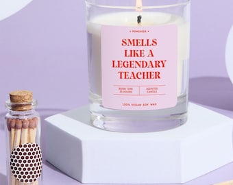 May include: A clear glass candle with a pink label that reads "Smells Like A Legendary Teacher." The candle is lit, and next to it is a small glass bottle filled with matches. The candle is made of 100% vegan soy wax and has a burn time of 25 hours.