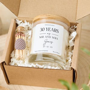 Op de afbeelding: Een cadeau set in een bruine doos, met een glazen kaars met een houten deksel en een kleine glazen fles met lucifers. Het kaarslabel luidt "30 YEARS as MR AND MRS Jones 27.12.25". De kaarsgeur is Cederhout & Jasmijn en brandt 25 uur.