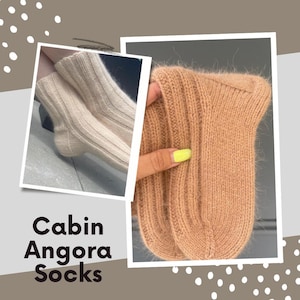 May include: The image shows two pairs of Angora socks. One pair is a light beige, the other is tan. The socks have a ribbed texture and look soft. The text "Cabin Angora Socks" is displayed in a bold font. The socks are likely made of a warm material.