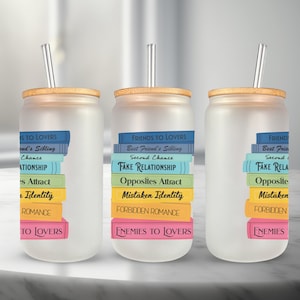 May include: Three frosted glass tumblers with bamboo lids and clear straws. Each tumbler has a stack of colourful book spines with text that reads "Friends to Lovers", "Best Friend's Sibling", "Second Chance", "Fake Relationship", "Opposites Attract", "Mistaken Identity", "Forbidden Romance", "Enemies to Lovers".
