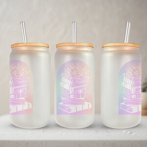May include: Three frosted glass tumblers with bamboo lids and silver straws. Each tumbler features a white illustration of books and flowers within a pastel rainbow arch. The tumblers are displayed on a white surface.