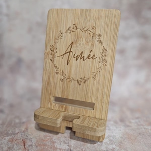 May include: A wooden phone stand with a floral wreath design and the name "Aimée" engraved on it.