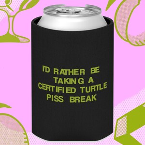 May include: Black can cooler with the text "I'd rather be taking a certified turtle piss break" in green letters.