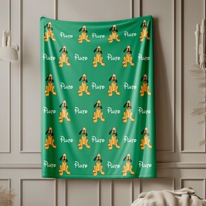 May include: A green blanket featuring a repeating pattern of the cartoon dog Pluto in a sitting position, alternating with the white text Pluto written in a cursive script. The blanket displays multiple rows of the character and the name across the fabric.