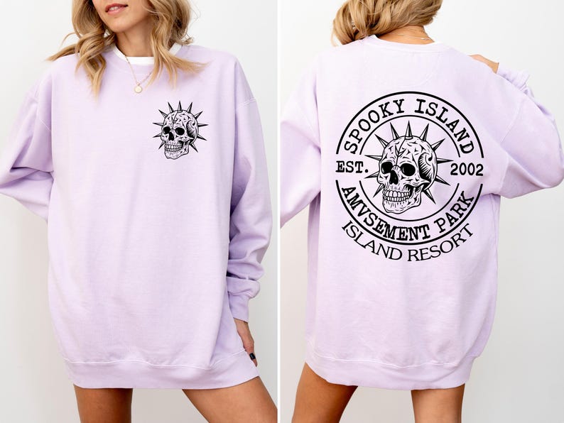 K&ouml;nnte beinhalten: Ein helllila Sweatshirt mit einem schwarzen Totenkopf-Motiv auf der Vorder- und R&uuml;ckseite. Das R&uuml;ckendesign ist ein kreisf&ouml;rmiges Design mit dem Text "Spooky Island Amusement Park Island Resort Est. 2002."