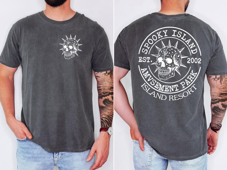 K&ouml;nnte beinhalten: Dunkelgraues T-Shirt mit einem wei&szlig;en Totenkopf-Motiv auf der Vorder- und R&uuml;ckseite. Auf der R&uuml;ckseite befindet sich ein kreisf&ouml;rmiges Design mit dem Text "Spooky Island Amusement Park Island Resort" und dem Jahr "2002".