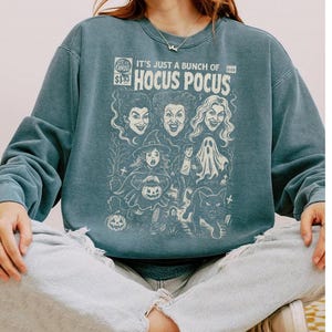 Może przedstawiać: Łupkowoniebieska bluza z okrągłym dekoltem i kremowym nadrukiem graficznym stylizowanym na okładkę komiksu vintage. Napis głosi IT'S JUST A BUNCH OF HOCUS POCUS, a całość uzupełniają ilustracje trzech kobiet, dziecka w kostiumie, ducha oraz kota.
