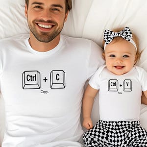 May include: White t-shirts with black graphic keyboard key designs. One shirt has "Ctrl + C" and "Copy" text, the other has "Ctrl + V" and "Paste". The baby wears a black and white checkered bottom and a matching bow.