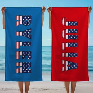 May include: Two beach towels, one blue and one red, are held up against a beach and sky backdrop. The blue towel spells out "RAYE" in a font that incorporates the American flag design. The red towel spells out "JULIA" in a similar style.