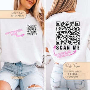 Peut inclure: Sweat-shirt blanc avec un code QR noir et blanc au dos. Le texte "SCAN ME" est écrit sous le code avec des flèches roses qui pointent vers lui. Le texte "YOUR CUSTOM OR CODE & CUSTOM TEXT" est écrit sous les flèches. Le sweat-shirt est porté par une personne portant un jean bleu.