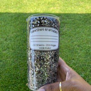 May include: A black and gold glitter tumbler with a white label that reads "DameShug Kraftables 100 Sheets - 200 Pages Wide Ruled".