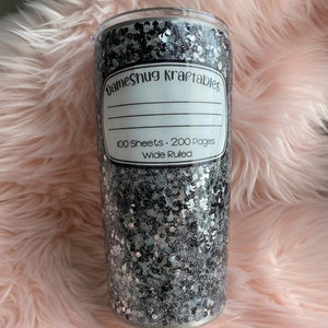 May include: A black and silver glitter tumbler with a white label that says "Dameshug Kraftables" and "100 Sheets. 200 Pages Wide Ruled".