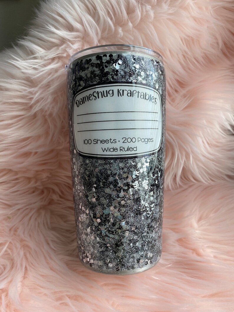 May include: A black and silver glitter tumbler with a white label that says "Dameshug Kraftables" and "100 Sheets. 200 Pages Wide Ruled".