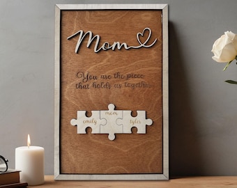 May include: Wooden sign with the words "Mom" and "You are the piece that holds us together."  The sign also features three puzzle pieces with the names "Emily", "Mom", and "Tyler" written on them.