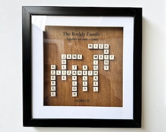 May include: A framed wood sign with the words "The Ruddy Family" and "Together we make a family" at the top. The names "Nick", "Jane", "Matt", and "Elizabeth" are spelled out using Scrabble tiles in a crossword puzzle format. The score is 120.