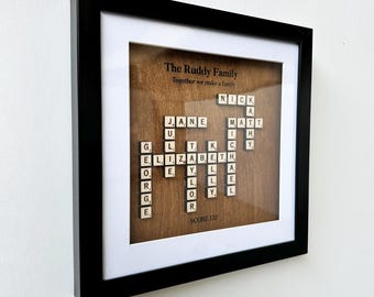 May include: A framed wood plaque with the words "The Ruddy Family" and "Together we make a family" at the top. The names "Jane", "Nick", "Matt", "Liz", "Elizabeth", "Julie", "Kyle", "Ollie", "George", "Lola", and "Rory" are spelled out in a crossword puzzle format using Scrabble tiles. The score is 120.