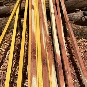 May include: A collection of long, thin wooden strips arranged vertically. The strips feature a mix of vibrant yellow and reddish-brown wood grain patterns, showcasing natural color variations and textures along their straight, narrow lengths.