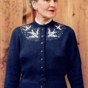 May include: A navy blue cardigan sweater with a white bird design on the shoulders. The sweater has a button-up front and is paired with a matching navy blue skirt. The woman in the image is holding a red book.