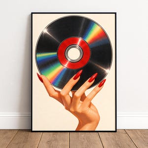 May include: A framed wall art print featuring a hand with long, bright red fingernails holding a circular compact disc. The disc has a black surface with a central red ring and a vibrant rainbow-colored light reflection across its metallic finish.