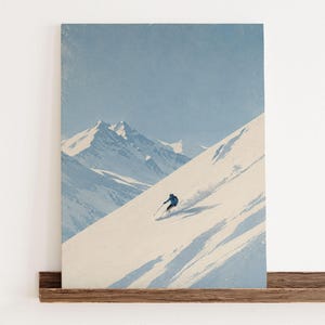 Könnte beinhalten: Ein rechteckiger Wandkunstdruck mit einer minimalistischen Illustration eines einzelnen Skifahrers in einer blauen Jacke, der einen steilen, schneebedeckten Berghang hinunterfährt. Der Hintergrund zeigt zerklüftete, schneebedeckte Gipfel.