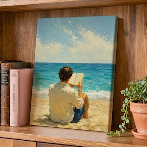 Könnte beinhalten: Ein rechteckiger Leinwanddruck, der eine Person zeigt, die an einem Sandstrand sitzt, auf den blauen Ozean blickt und ein offenes Buch liest. Die Person trägt ein helles Hemd und eine dunkle Shorts. Der Himmel ist hellblau mit weißen Wolken.