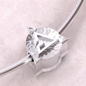 Könnte beinhalten: Ein silbernes Armband mit einem runden, strukturierten Anhänger mit einem weißen Dreiecksdesign.