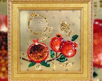 May include: A framed mosaic artwork featuring three pomegranates, a branch with leaves, and a circular inscription in Hebrew. The pomegranates are made of red, orange, and amber colored glass pieces. The background is gold.