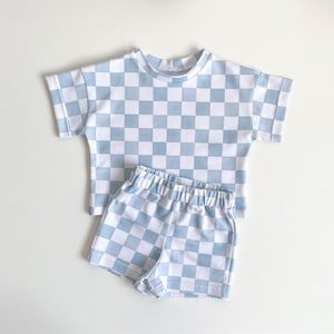 May include: A blue and white checkered short-sleeved shirt and shorts set for children. The fabric has a light blue and white checkered pattern.