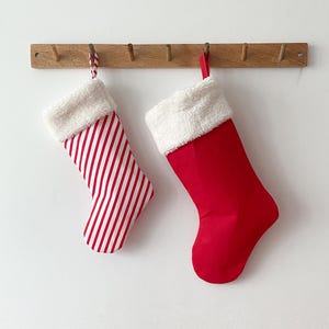 May include: Two Christmas stockings hanging on a wooden rack. One stocking is red with white stripes, and the other is solid red. Both have white faux fur cuffs.