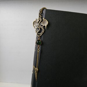 May include: A gold dragon bookmark with a green gemstone and a spear-shaped tip.