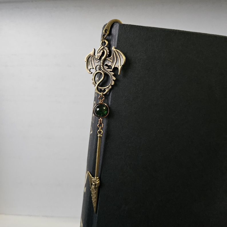 May include: A gold dragon bookmark with a green gemstone and a spear-shaped tip.