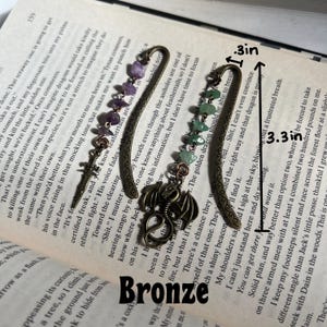 May include: A bronze dragon bookmark with amethyst and green gemstone accents. The bookmark is 3.3 inches long and 1 inch wide. The bookmark is labeled "Bronze".