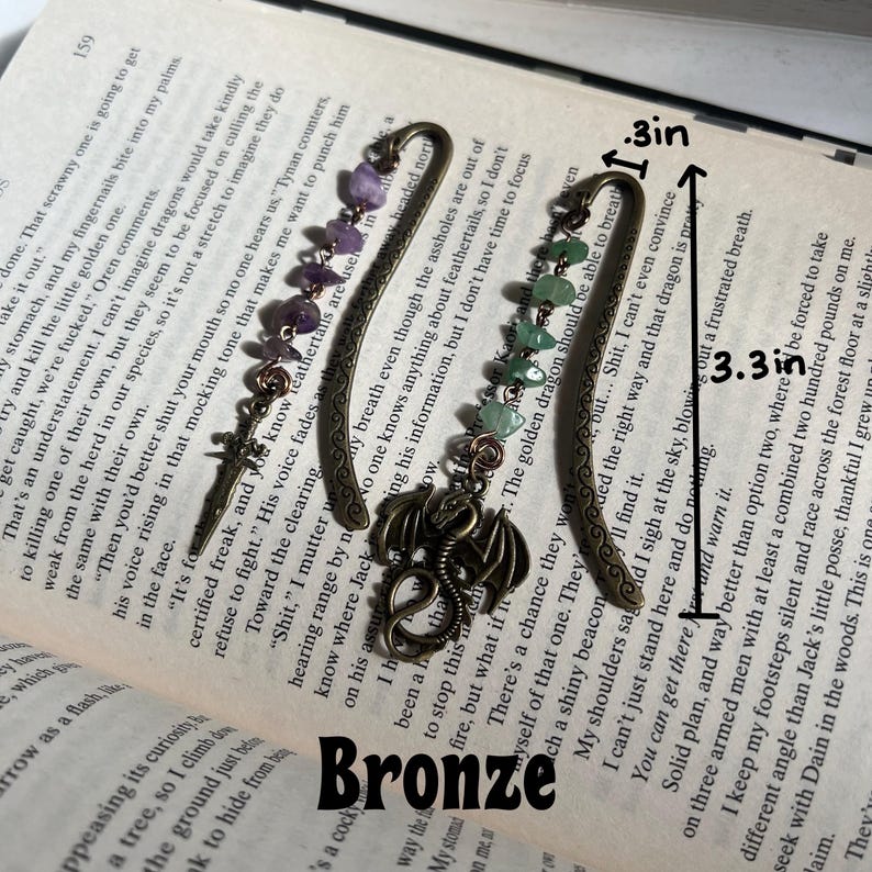 May include: A bronze dragon bookmark with amethyst and green gemstone accents. The bookmark is 3.3 inches long and 1 inch wide. The bookmark is labeled "Bronze".