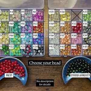 May include: A clear plastic storage box filled with various colored beads. The beads are numbered 1 through 47. There are two smaller dishes with red and dark green beads, labeled "RED" and "DARK GREEN". The text "Choose your bead" is printed below the storage box.