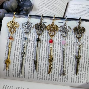 May include: Six gold, silver, and bronze dragon bookmarks with red, green, and pink gemstones. Each bookmark features a dragon with a sword and a key.