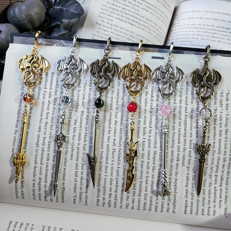 May include: Six gold, silver, and bronze dragon bookmarks with red, green, and pink gemstones. Each bookmark features a dragon with a sword and a key.
