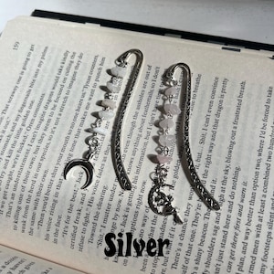 May include: Two silver bookmark with a crescent moon charm and pink and white stones. The bookmarks are decorated with intricate designs.