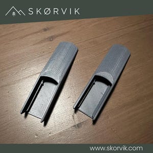 May include: Two identical grey, elongated, semi-cylindrical plastic components with a hollow, rectangular channel running along the underside. The exterior surface features a fine, layered texture consistent with 3D printing, and the top is rounded.